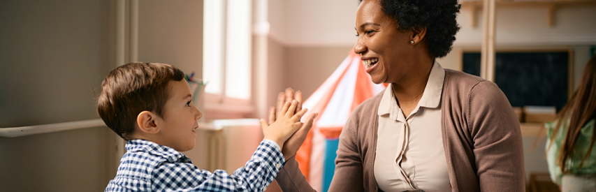 Cuidadora sorridente interage com criança em ambiente educacional lúdico, promovendo vínculo e aprendizado.